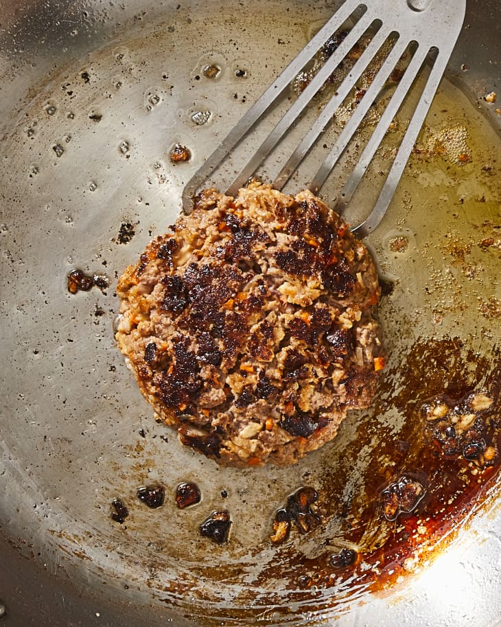 Meatloaf burger being cooked in a pan with a metal spatula