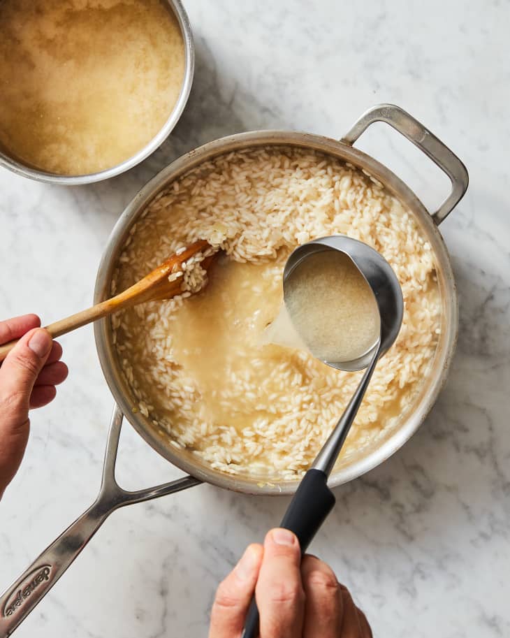 Overhead photo of someone ladeling broth into rice in the process of making vegan risotto