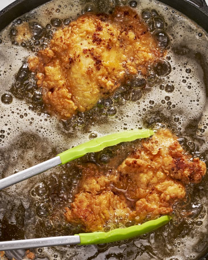 chicken frying in oil  being turned by tongs