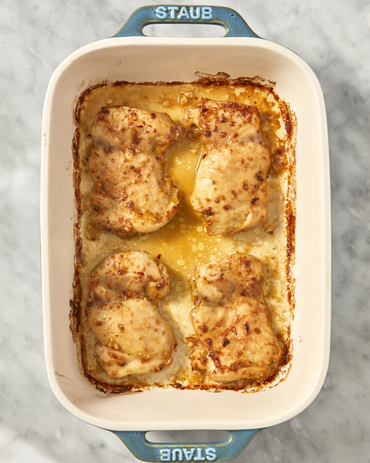 Overhead image of baked chicken thighs placed in a casserole dish on a marble surface