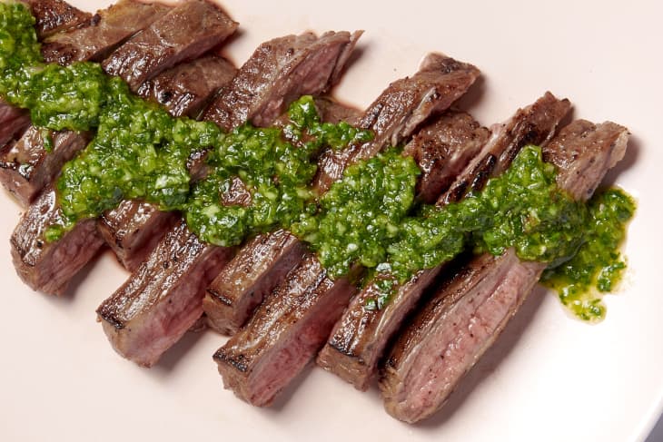 a sliced steak with green chimichurri sauce on it on a pink plate