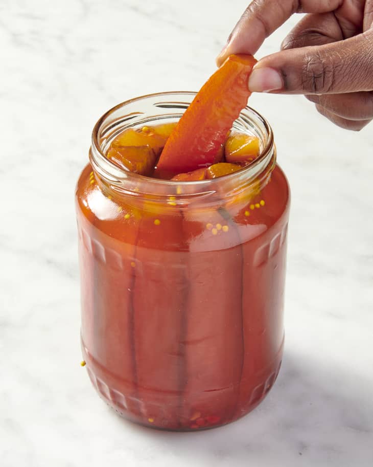 an open jar of pickle spears that has been infused with red Kool Aid with one spear being taken out by hand