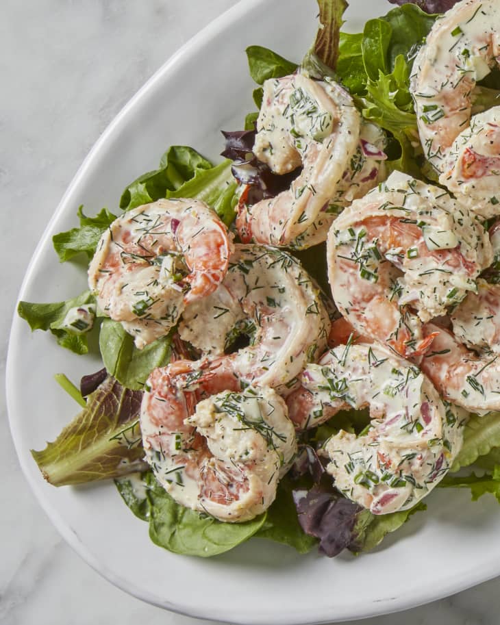 A platter of shrimp salad on top of greens on a marble surface.
