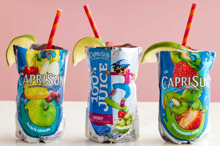 Three Capri Sun punch pouches with lime garnish and pink and orange straws on a marble surface with a pink background