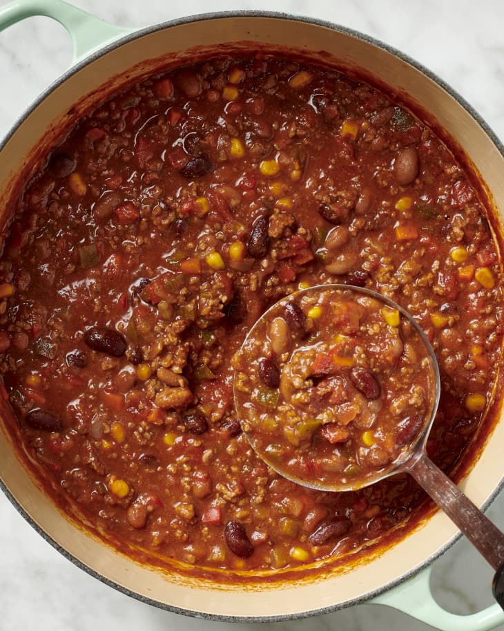 photo of a dutch oven full of chili with a ladle in it on a marble countertop