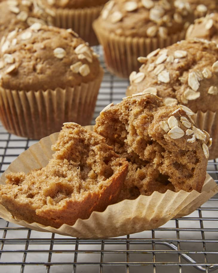 A close up of an applesauce muffin, unwrapped and split open on a cooling rack with whole muffins in the background