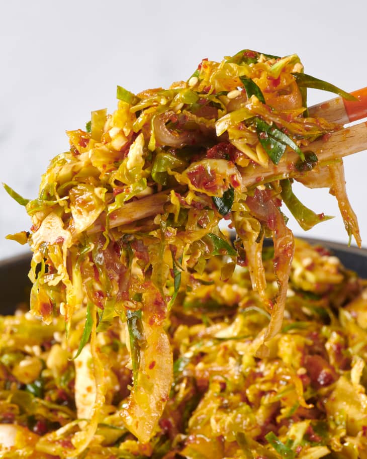 Someone using chopsticks to pick up Brussels sprout kimchi