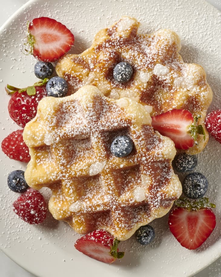 photo of liege waffles topped with assorted berries and powdered sugar on a white plate