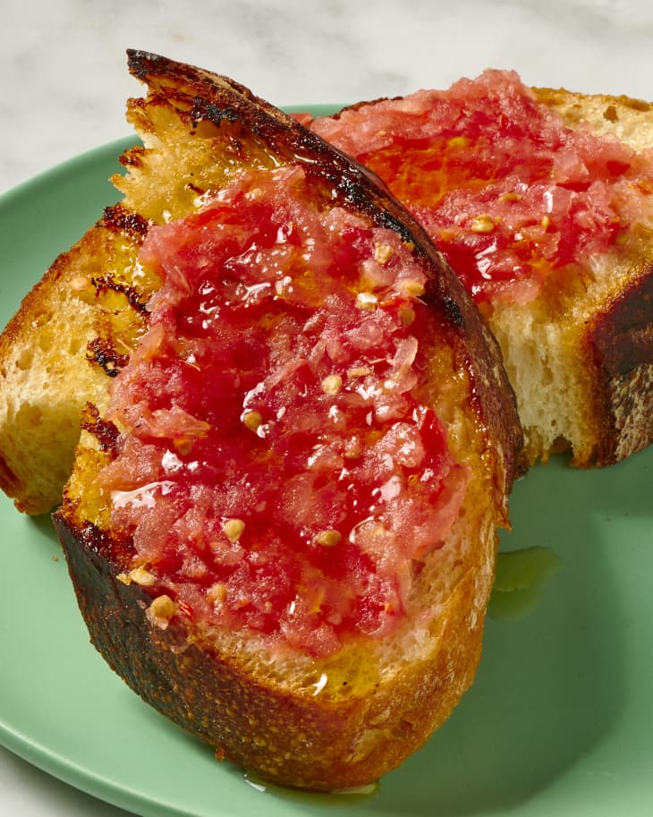 2 slices of pan con tomate on a green plate on a marble surface