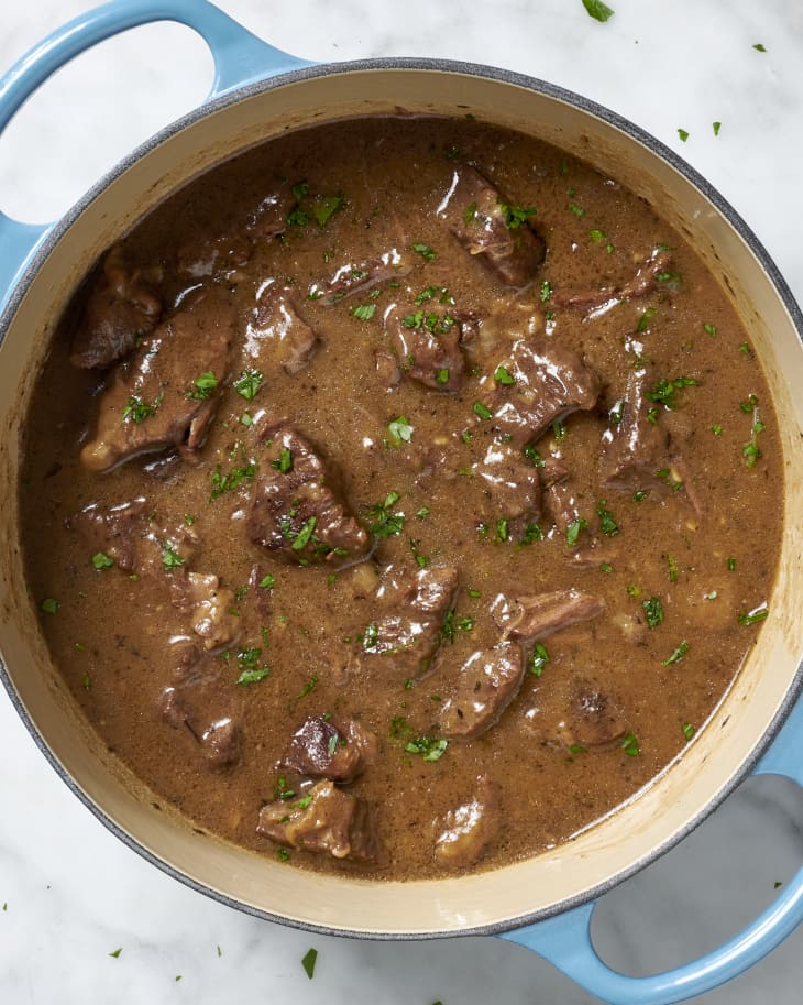 Overhead view of beef tips in a pot with blue handles topped with herbs.