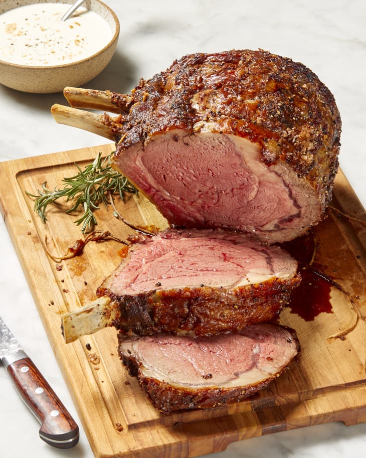 Angled view of prime rib resting on a wooden cutting board, first two slices are cut.