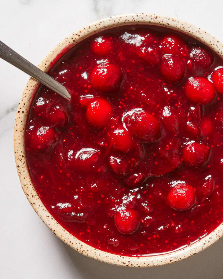 Overhead view of cranberry sauce in a white and brown speckled bowl with a spoon in the bowl.