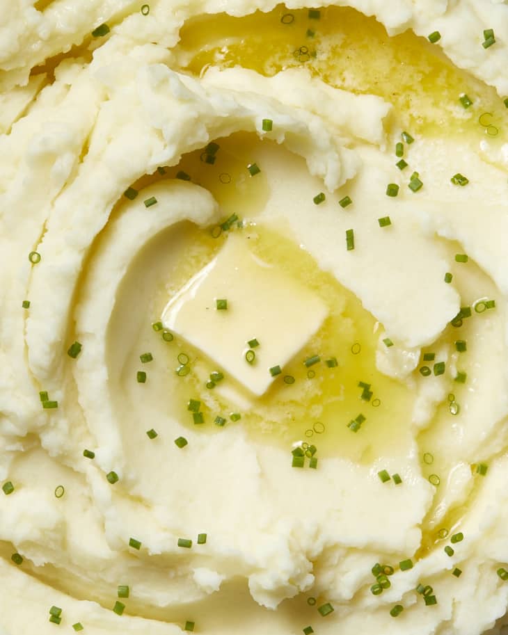 Close up view of mashed potatoes topped with chives and a pat of butter.