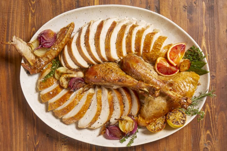 Overhead view of sliced turkey on a beige and brown ceramic platter with roasted blood orange slices, onions and herbs.
