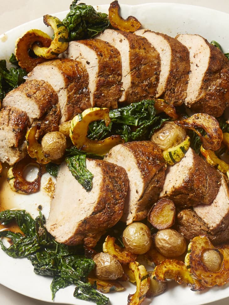 Overhead view of cooked, sliced pork tenderloin on a white oval platter on a bed of roasted squash, potatoes and spinach.