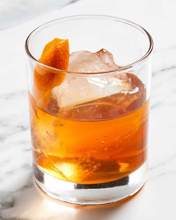 Angled view of an old fashioned in a rocks glass over ice with an orange peel in the glass.