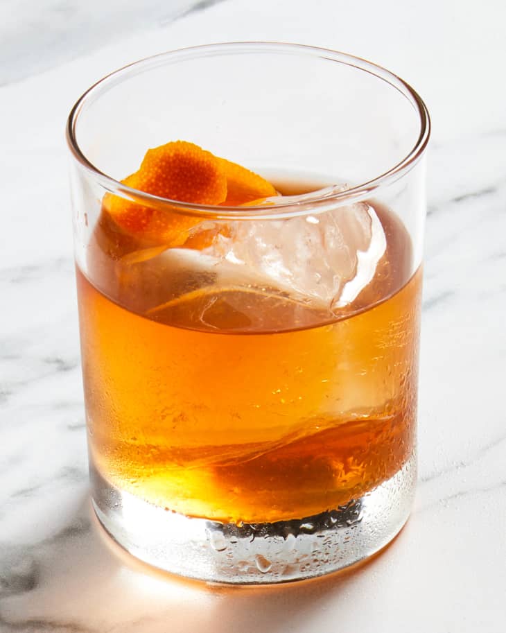 Angled view of an old fashioned in a rocks glass over ice with an orange peel in the glass.