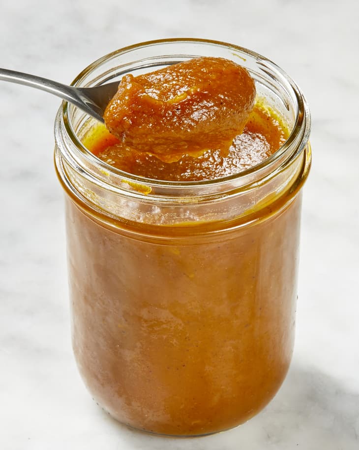 Overhead view of a scoop of pumpkin butter on a spoon, and the top of the glass jar of pumpkin butter.