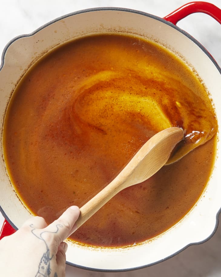 Overhead view of a wooden spoon stirring gravy in a red pot.