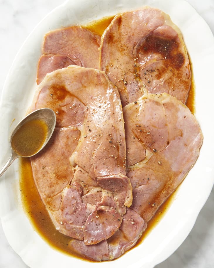 Overhead view of gravy poured onto ham, with a spoon of gravy resting on the white plate.