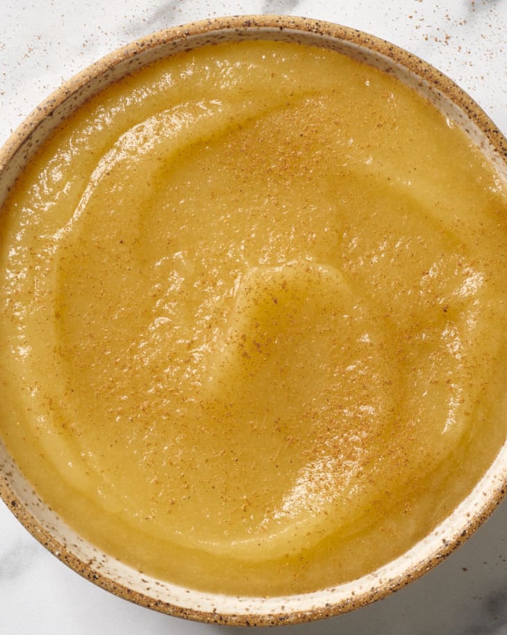 Close up, overhead view of applesauce topped with cinnamon in a white speckled bowl.