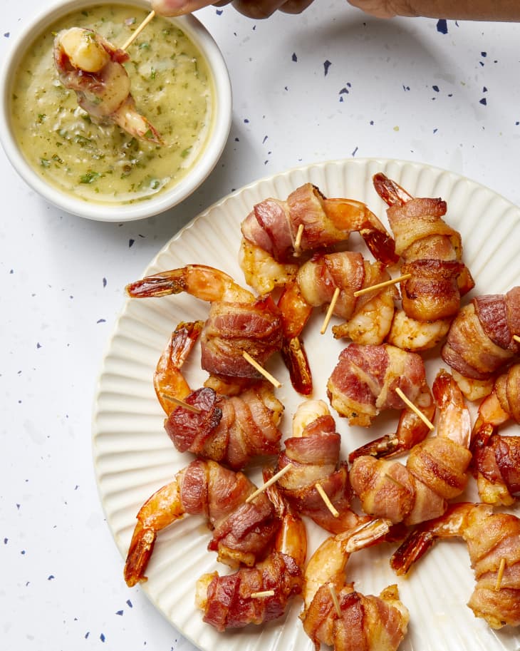 A platter of bacon wrapped shrimp with one being dipped into a compound butter.