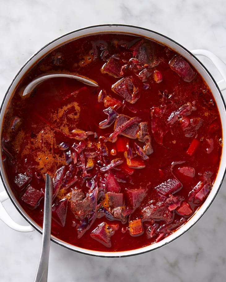 Overhead view of borscht in a white pot with a silver ladle resting in it.