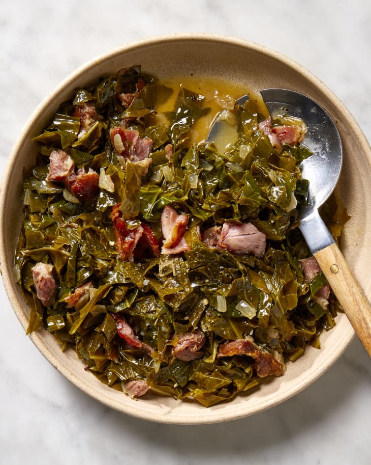 Overhead view of collard greens in a shallow, beige bowl, and a metal and wood serving spoon resting in the bowl.