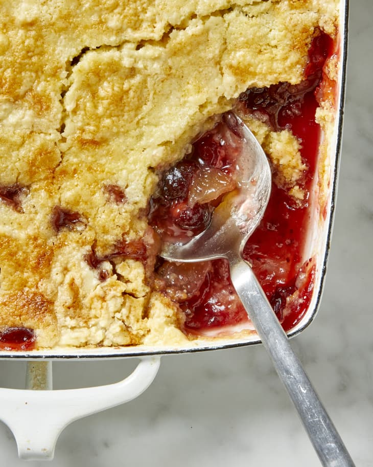 Overhead view of the dump cake in a white pan, with a big scoop taken out of the bottom right corner, and a serving spoon resting there.