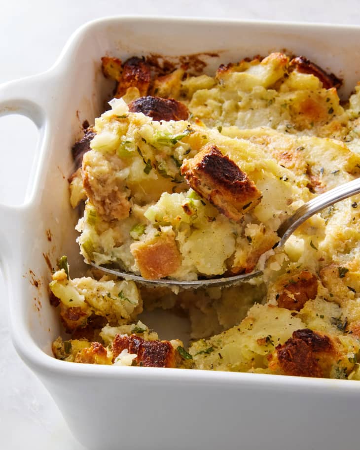 Potato stuffing in a casserole baking dish with a spoon scooping out a serving.