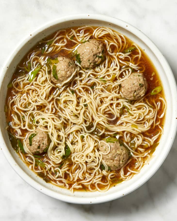 Overhead view of noodle soup with meat balls in a white bowl.