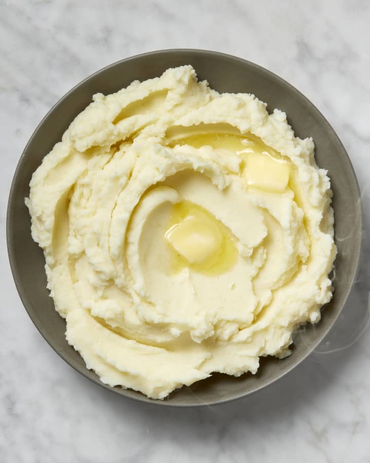 Overhead view of mashed potatoes in a grey bowl, topped with a pat of butter.
