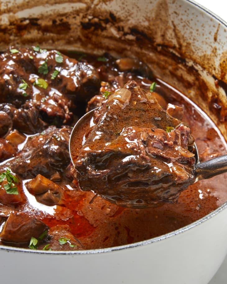 Angled shot of beef bourguignon in a white pot with a serving spoon scooping some out.