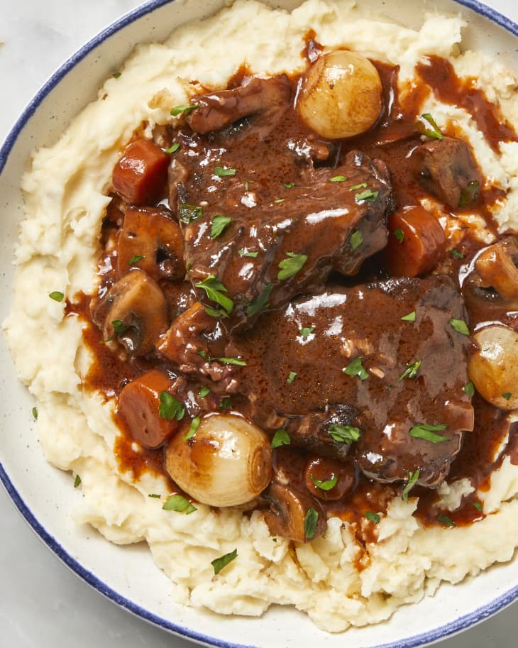 Overhead shot of beef bourguignon over mashed potatoes in a white bowl with blue trim.