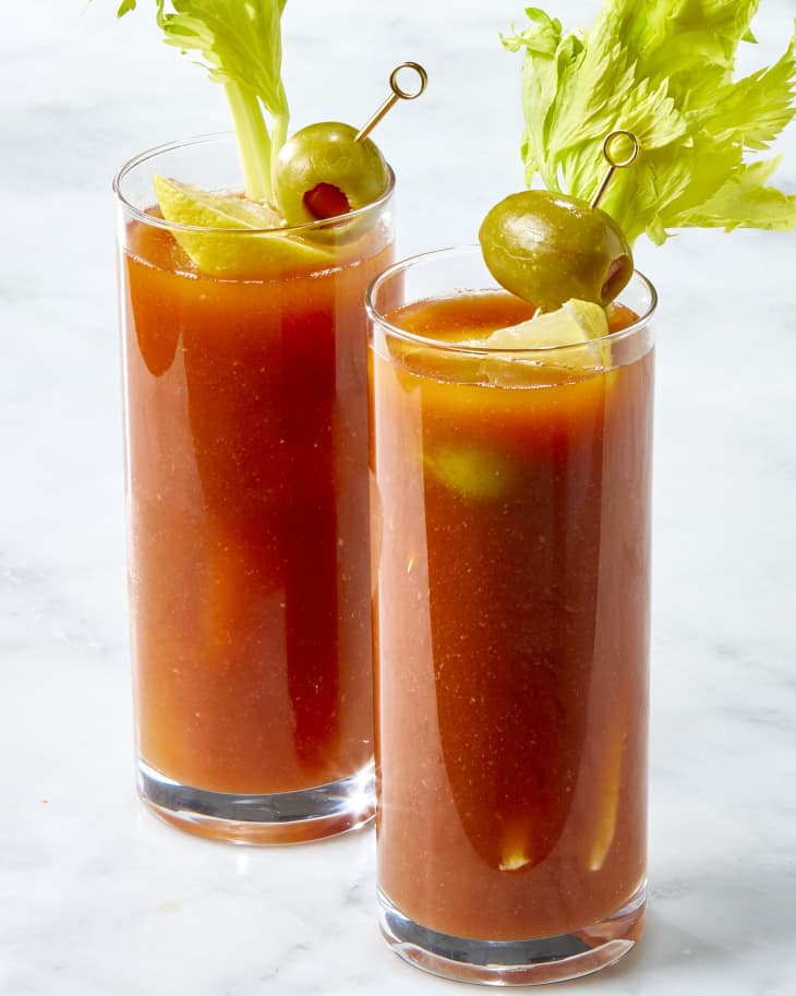Head on shot of two glasses of bloody mary's, garnished with lemon, olives and celery.