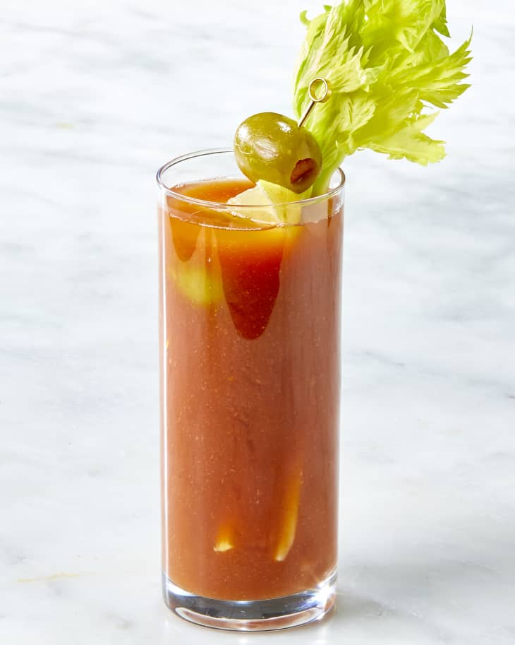 Head on shot of a single bloody mary, garnished with lemon, olives and celery.