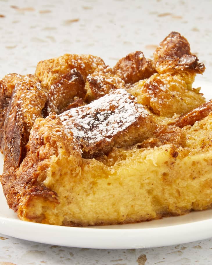 Head on shot of a piece of bread pudding on a small white plate resting on a white terrazzo surface.
