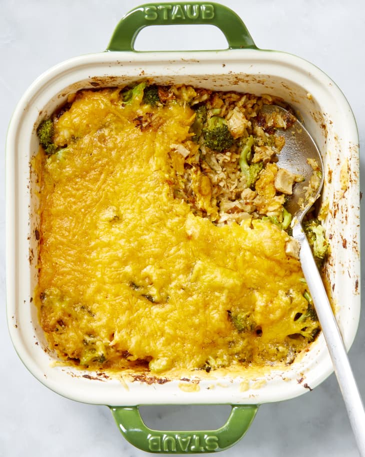 Overhead shot of the chicken, rice and broccoli casserole in a green and white casserole dish,  with the top right corner scoop missing.