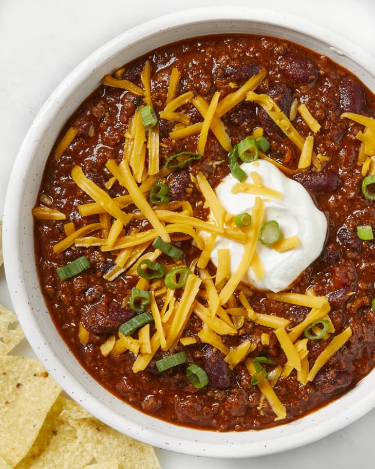 Overhead shot of chili in a white bowl, topped with sour cream, cheddar cheese and green onions.