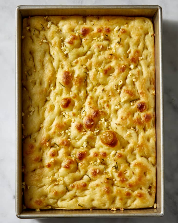 Close up of baked focaccia topped with herbs and garlic, in a metal loaf pan.