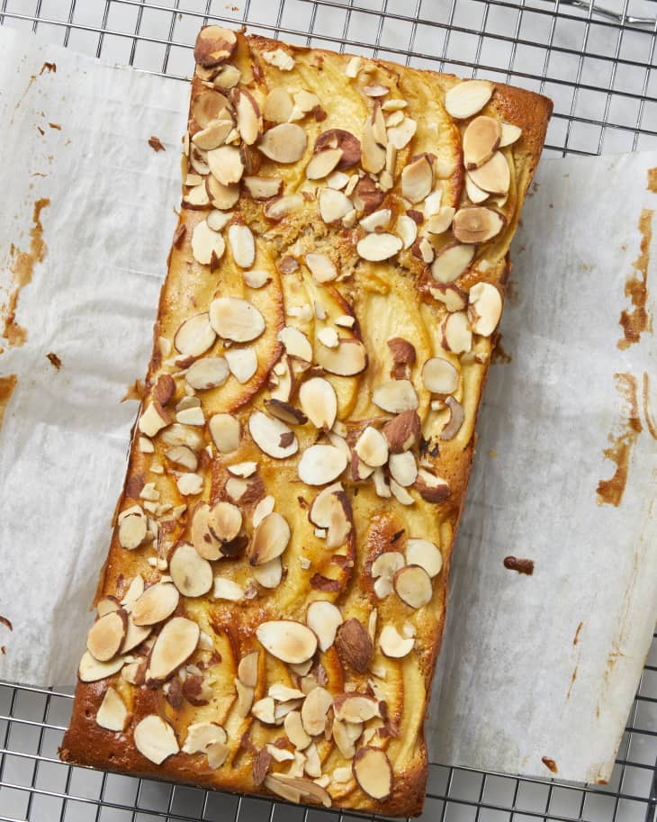 Overhead view of a whole apple cake topped with almonds on a cooling rack.