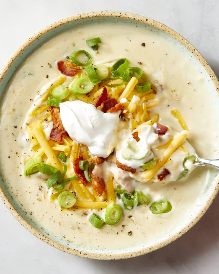 Overhead shot of a bowl of potato soup, topped with shredded cheese, sour cream, bacon and chives.