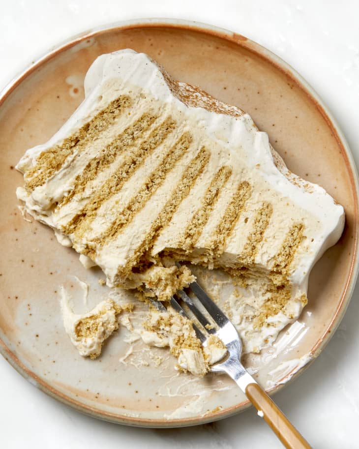 Overhead shot of a slice of pumpkin icebox cake with a bite taken out of it. The slice is on a beige and orange ceramic plate with a fork resting on the bottom right of the plate.