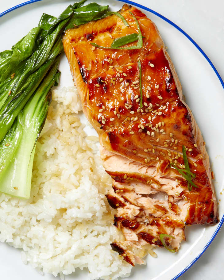 Overhead shot of a white plate with a blue trim, with a piece of teriyaki salmon, white rice and bok choy.