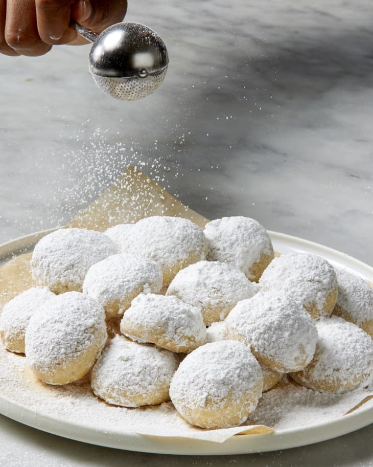 Head on shot of snowball cookies being dusted in powdered sugar.