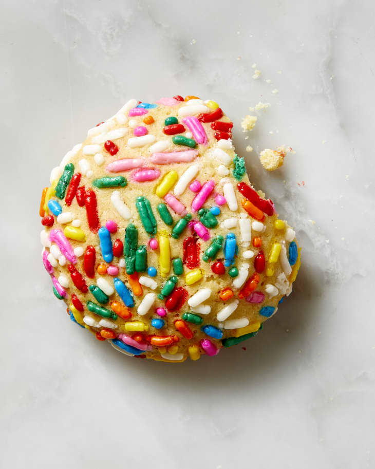 overhead view of a single sprinkle cookie on a marble surface with a bite taken out of it.