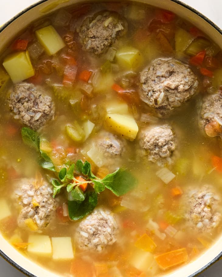 Overhead shot of albondigas soup in a large yellow pot, on a white marble surface.