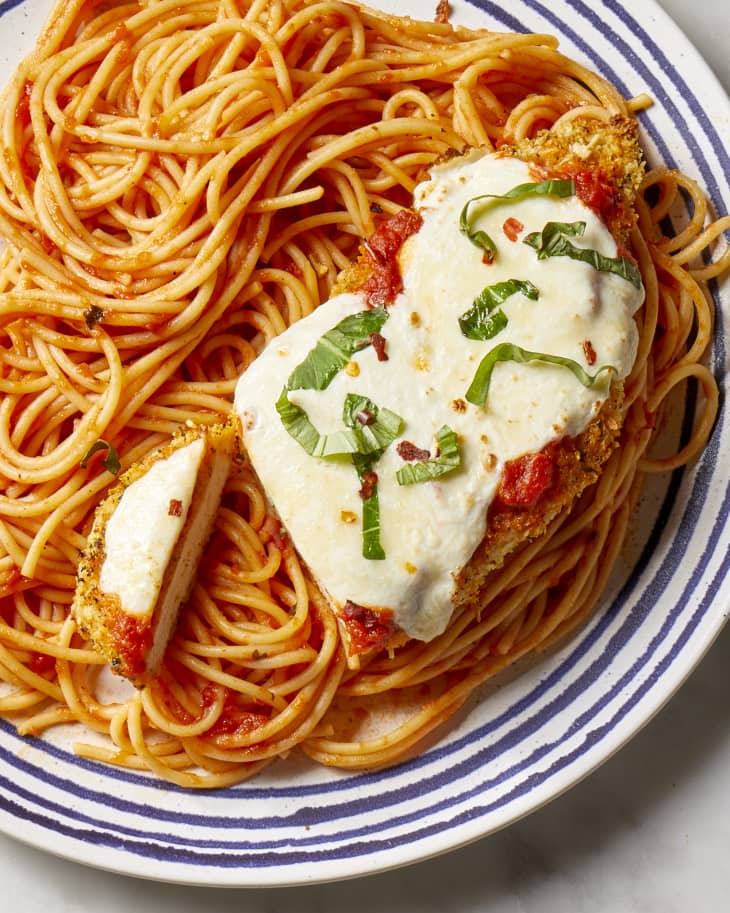 Overhead shot of chicken parmesan served over spaghetti on a blue and white striped plate.