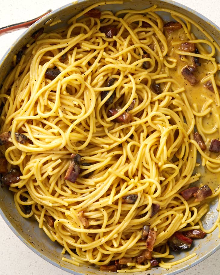 Overhead shot of carbonara in a grey pan, on a white surface.
