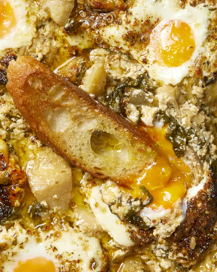 Overhead shot of a baguette resting in the spinach artichoke baked egg yolk.